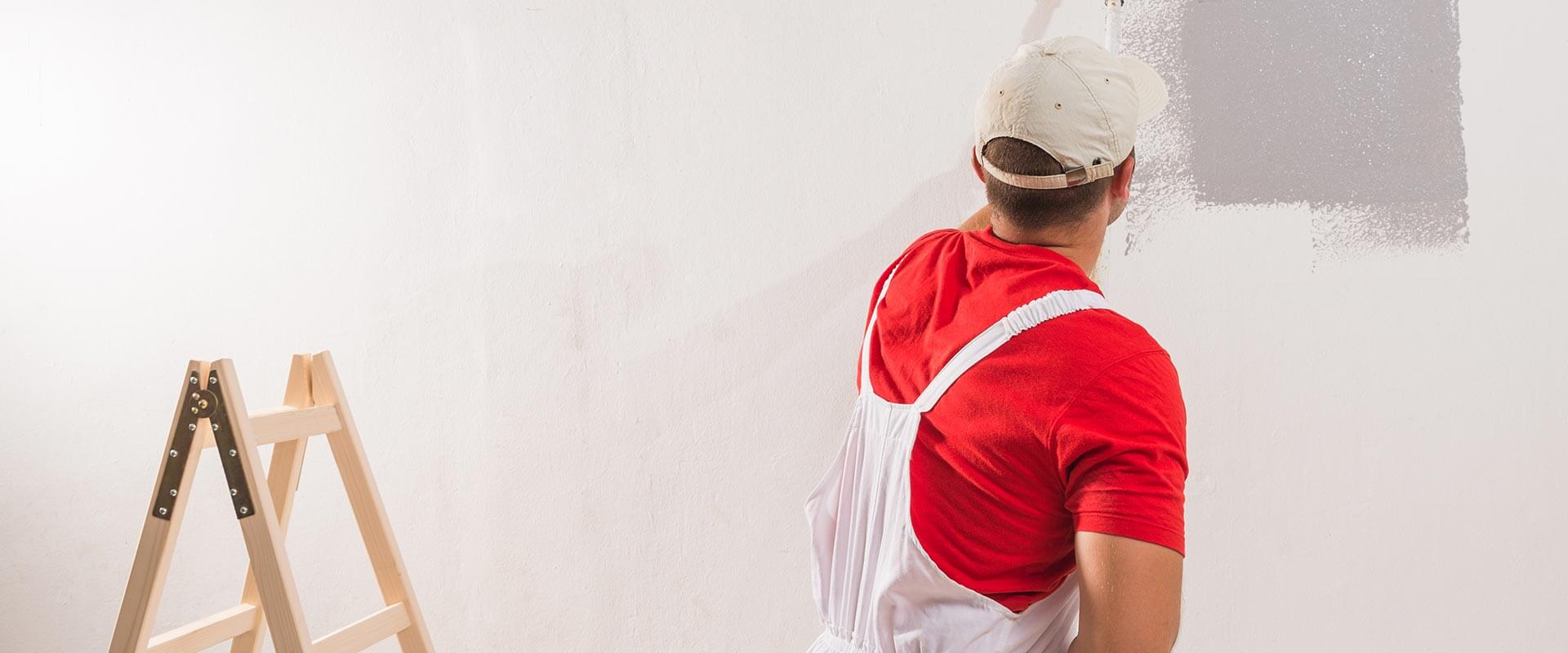 Un homme portant une chemise blanche et un tablier rouge peint un mur avec un pinceau.